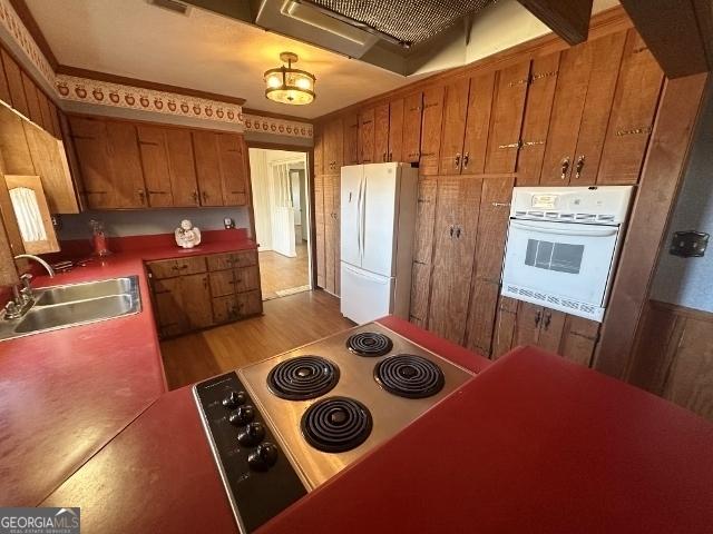 kitchen with range hood, wood walls, sink, light wood-type flooring, and white appliances