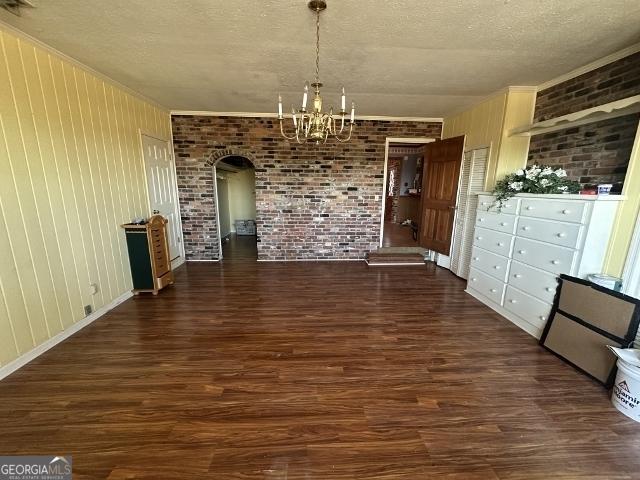 unfurnished dining area featuring brick wall, dark hardwood / wood-style floors, crown molding, a textured ceiling, and an inviting chandelier