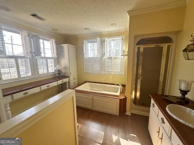 bathroom with hardwood / wood-style flooring, vanity, ornamental molding, a textured ceiling, and separate shower and tub