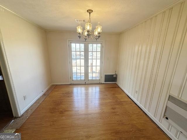 unfurnished dining area featuring crown molding, wood-type flooring, a chandelier, and french doors