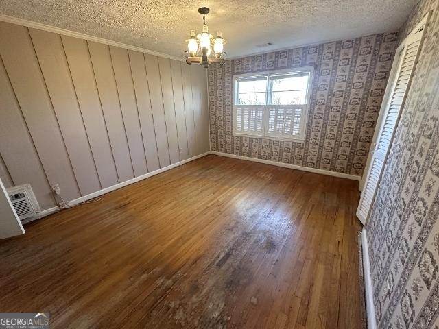 unfurnished dining area with ornamental molding, a chandelier, hardwood / wood-style floors, and a textured ceiling