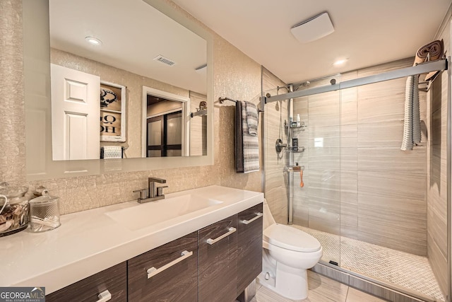 bathroom with vanity, toilet, a shower with door, and backsplash