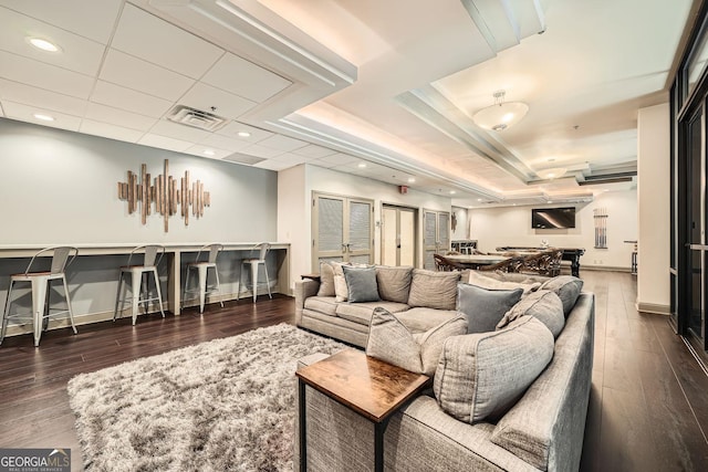 living room with dark wood-type flooring, indoor bar, a tray ceiling, and a paneled ceiling