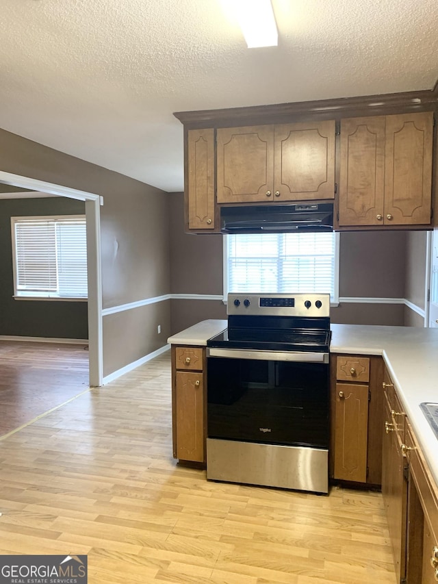 kitchen with light countertops, electric range, under cabinet range hood, and light wood-style flooring