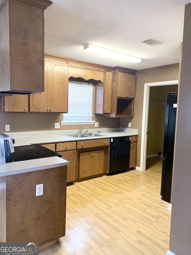 kitchen with black appliances, light countertops, light wood finished floors, and a sink