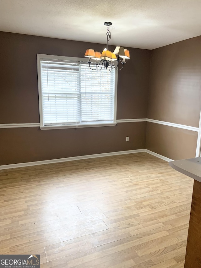 spare room featuring a chandelier, baseboards, and light wood finished floors