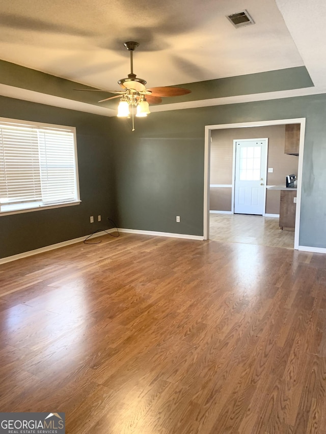 empty room with hardwood / wood-style flooring, ceiling fan, and a raised ceiling