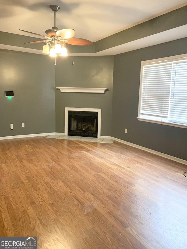 unfurnished living room featuring baseboards, wood finished floors, ceiling fan, and a fireplace with flush hearth