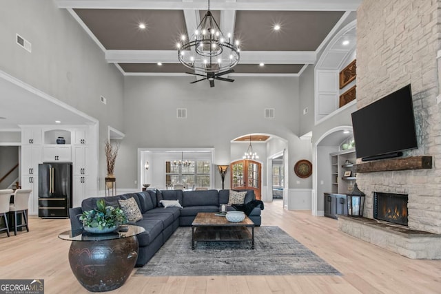 living room featuring a fireplace, beamed ceiling, ornamental molding, a notable chandelier, and light hardwood / wood-style flooring