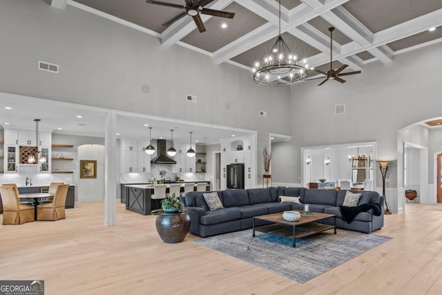 living room with coffered ceiling, crown molding, light wood-type flooring, beam ceiling, and ceiling fan with notable chandelier