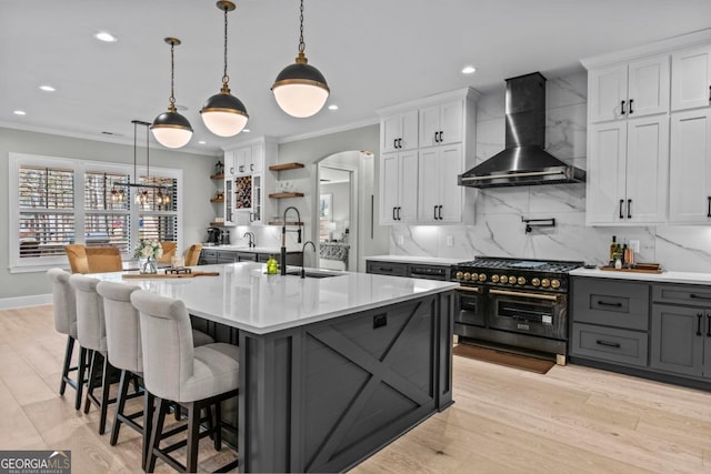 kitchen with pendant lighting, wall chimney range hood, white cabinetry, backsplash, and range with two ovens