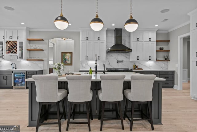 kitchen with wall chimney exhaust hood, beverage cooler, and white cabinets