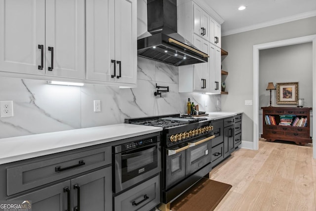 kitchen with tasteful backsplash, white cabinets, range with two ovens, ornamental molding, and wall chimney range hood