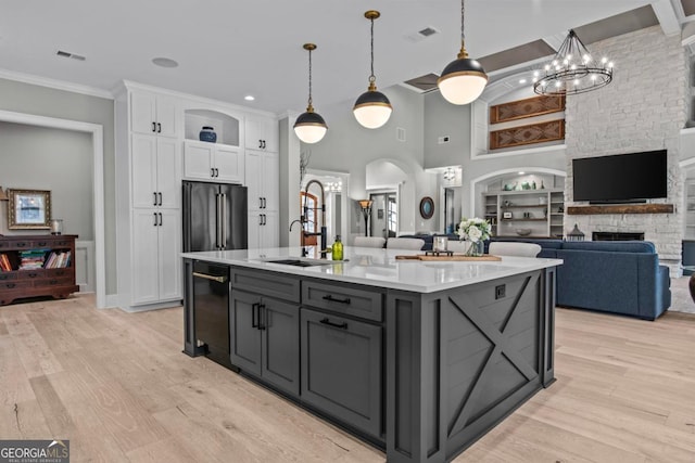 kitchen featuring decorative light fixtures, a center island with sink, light wood-type flooring, high quality fridge, and white cabinets