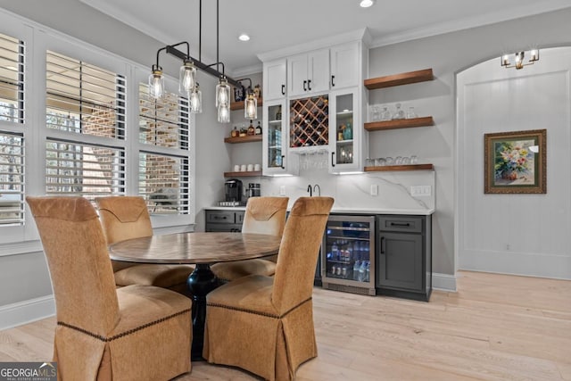 dining area featuring wine cooler, light hardwood / wood-style flooring, ornamental molding, and bar area