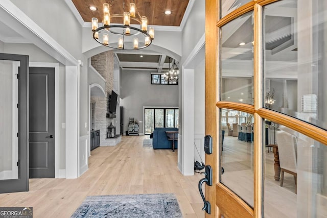 foyer featuring beam ceiling, a high ceiling, light hardwood / wood-style floors, a large fireplace, and a chandelier