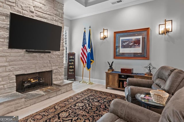 living room with crown molding, a stone fireplace, and light hardwood / wood-style floors