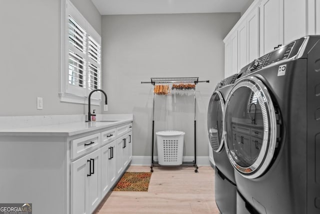 clothes washing area featuring cabinets, separate washer and dryer, sink, and light hardwood / wood-style flooring