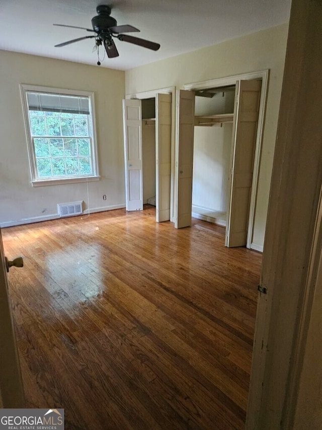 unfurnished bedroom with baseboards, visible vents, a ceiling fan, wood-type flooring, and multiple closets