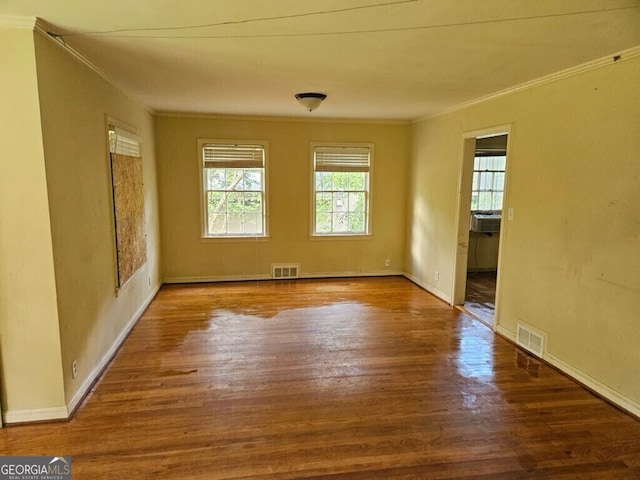 empty room with ornamental molding, wood finished floors, and visible vents