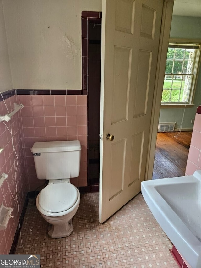 bathroom featuring visible vents, wainscoting, tile walls, and toilet