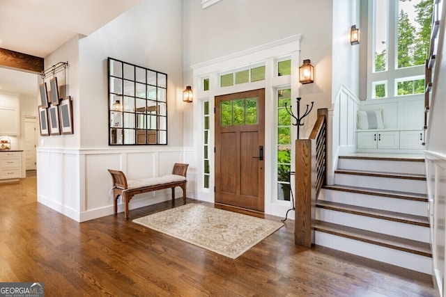 entrance foyer featuring a decorative wall, a high ceiling, wood finished floors, stairs, and wainscoting