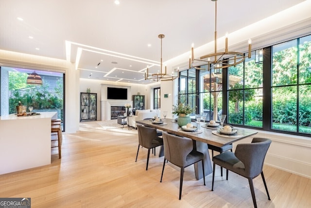 dining area with light wood-style floors, recessed lighting, a glass covered fireplace, and a notable chandelier