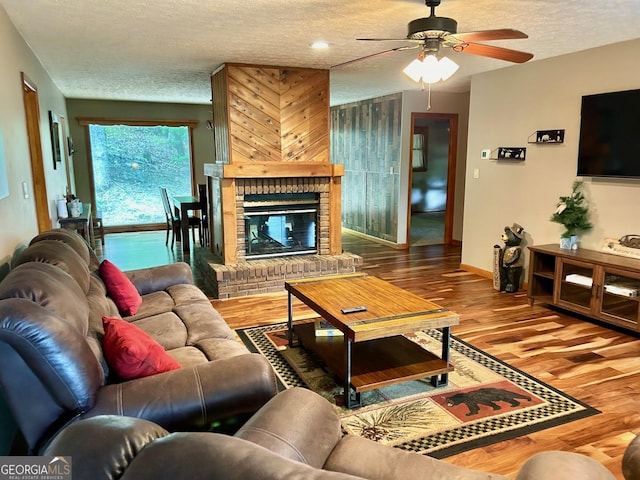 living room with ceiling fan, hardwood / wood-style floors, a brick fireplace, and a textured ceiling