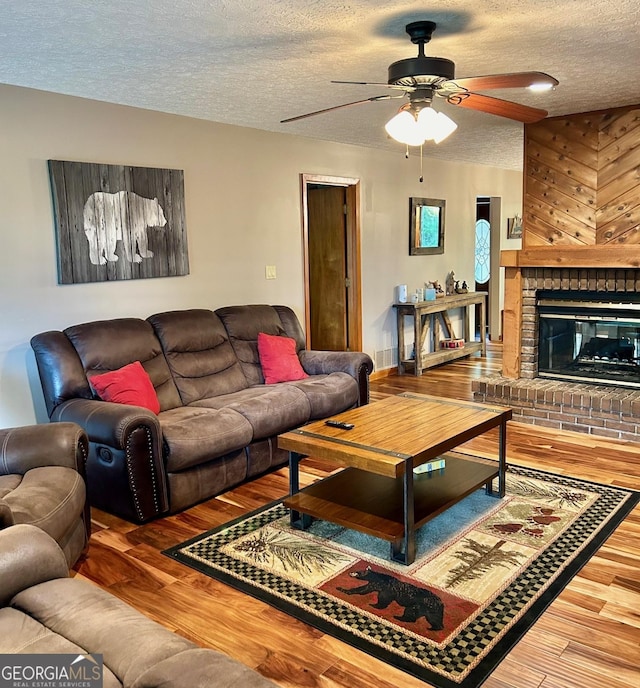 living room with wood-type flooring, a brick fireplace, ceiling fan, and a textured ceiling