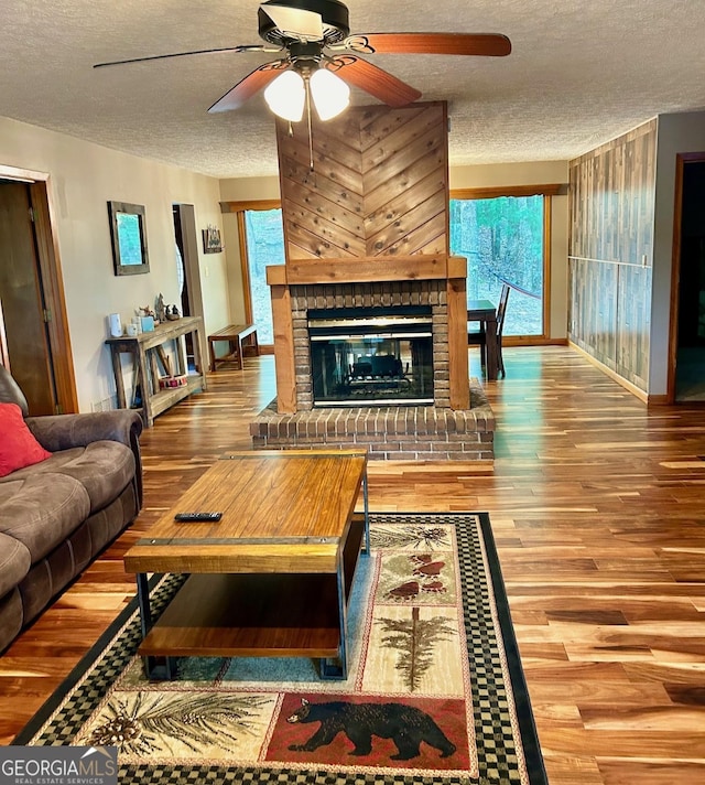 living room featuring wood-type flooring, a brick fireplace, ceiling fan, and a textured ceiling