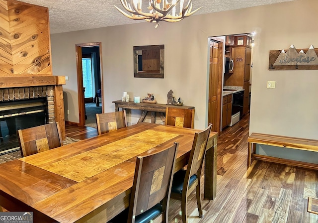 dining room with a notable chandelier, hardwood / wood-style flooring, a fireplace, and a textured ceiling