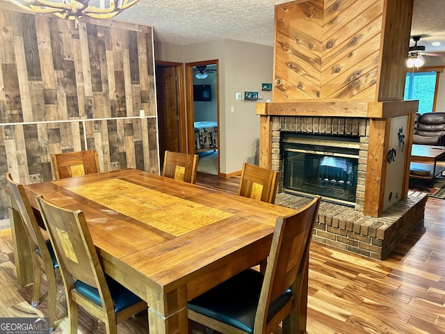 dining space featuring ceiling fan, a brick fireplace, a textured ceiling, and light hardwood / wood-style floors