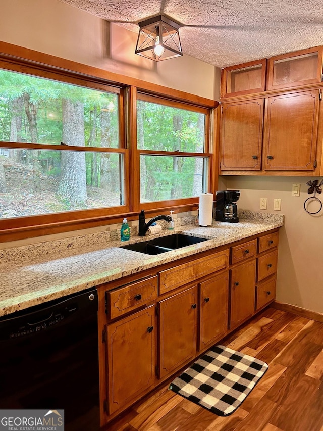 kitchen with dishwasher, wood-type flooring, sink, light stone counters, and a textured ceiling