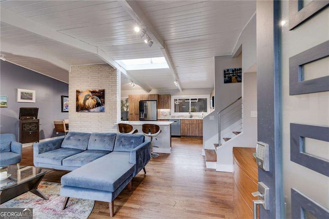 living room featuring track lighting, light hardwood / wood-style flooring, and vaulted ceiling with beams