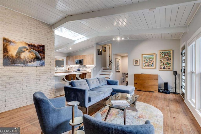 living room with brick wall, vaulted ceiling with beams, and light hardwood / wood-style floors