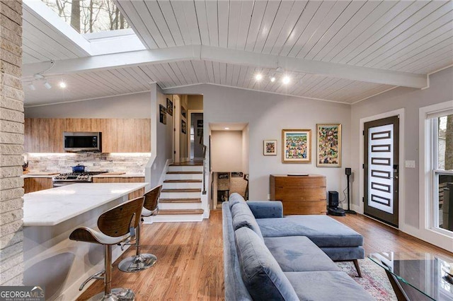 living room with vaulted ceiling with skylight, light hardwood / wood-style floors, and wooden ceiling