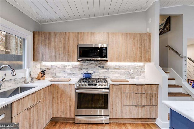 kitchen with vaulted ceiling, appliances with stainless steel finishes, sink, backsplash, and light hardwood / wood-style floors