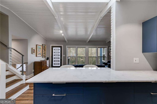 kitchen with blue cabinets, light stone countertops, dark wood-type flooring, and beam ceiling