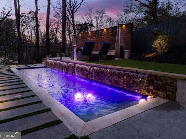 pool at dusk with pool water feature and a patio area