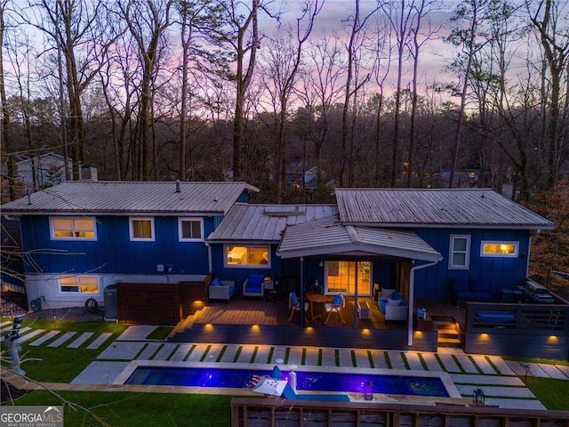 back house at dusk with a pool side deck and an outdoor hangout area