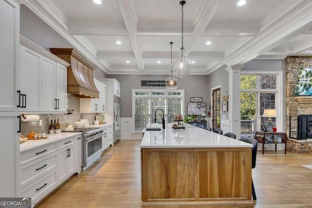 kitchen featuring pendant lighting, high quality appliances, white cabinetry, an island with sink, and beamed ceiling