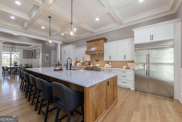 kitchen featuring white cabinetry, a spacious island, built in fridge, and custom range hood