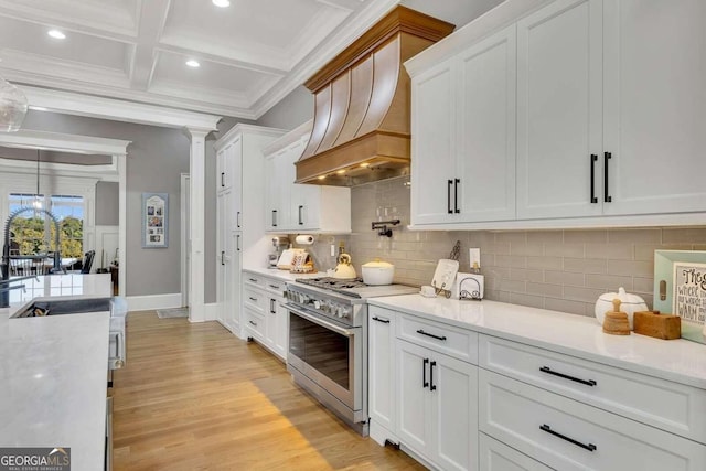 kitchen featuring custom exhaust hood, white cabinetry, crown molding, high end stainless steel range oven, and light hardwood / wood-style floors