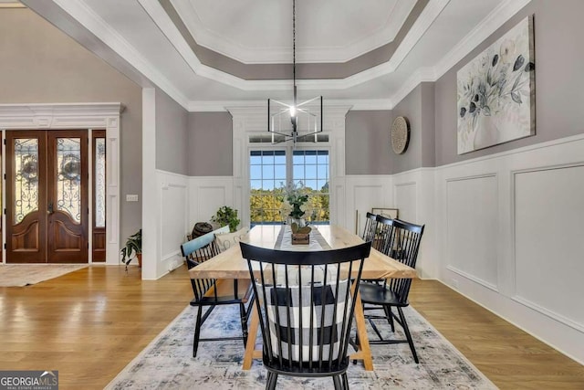 dining room with french doors, crown molding, a chandelier, light hardwood / wood-style flooring, and a raised ceiling