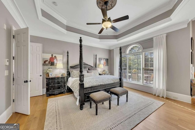 bedroom featuring crown molding, a raised ceiling, ceiling fan, and light wood-type flooring