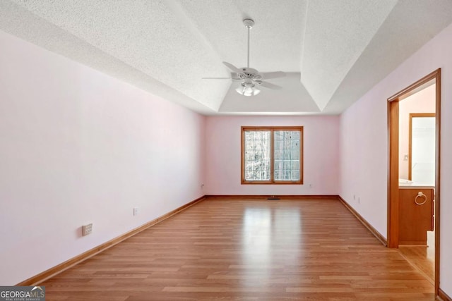 spare room featuring ceiling fan, a tray ceiling, light hardwood / wood-style floors, and a textured ceiling