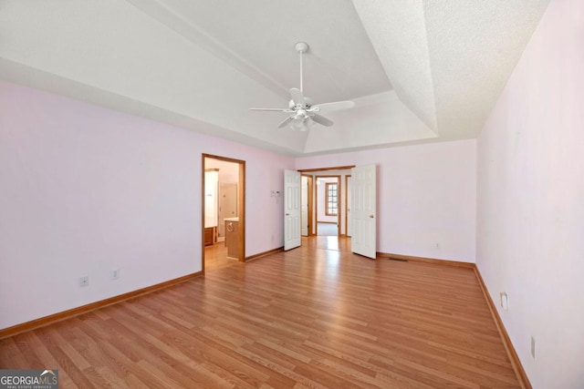 interior space with ceiling fan, a tray ceiling, and light wood-type flooring