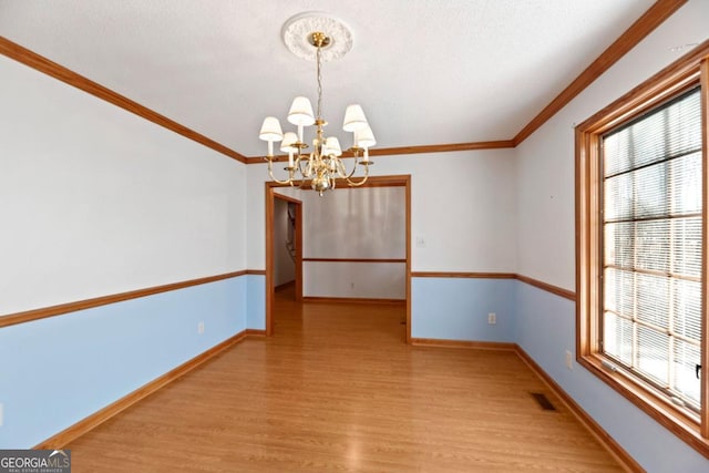 unfurnished dining area with crown molding, plenty of natural light, a chandelier, and light hardwood / wood-style flooring