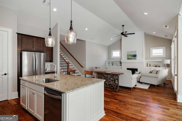 kitchen featuring sink, light stone counters, dark brown cabinets, stainless steel refrigerator, and a kitchen island with sink