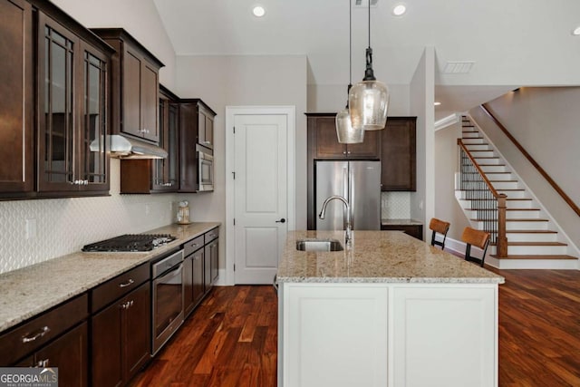 kitchen with stainless steel appliances, sink, light stone counters, and dark brown cabinetry